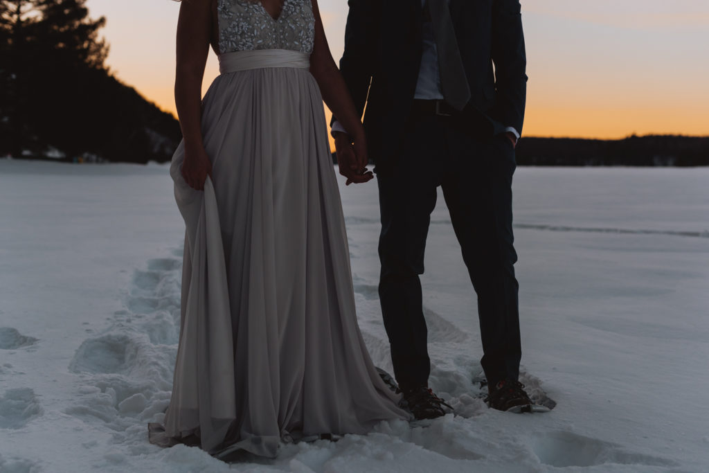 bride and groom snowshoeing on frozen lake at winter during sunset