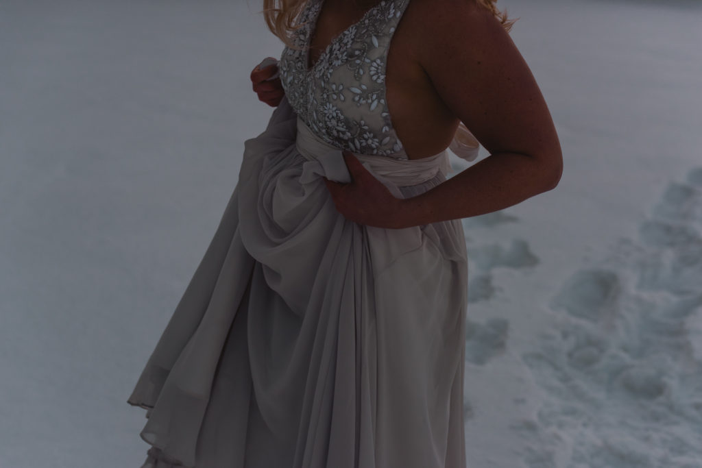 bride holding her dress walking through the snow at sunset