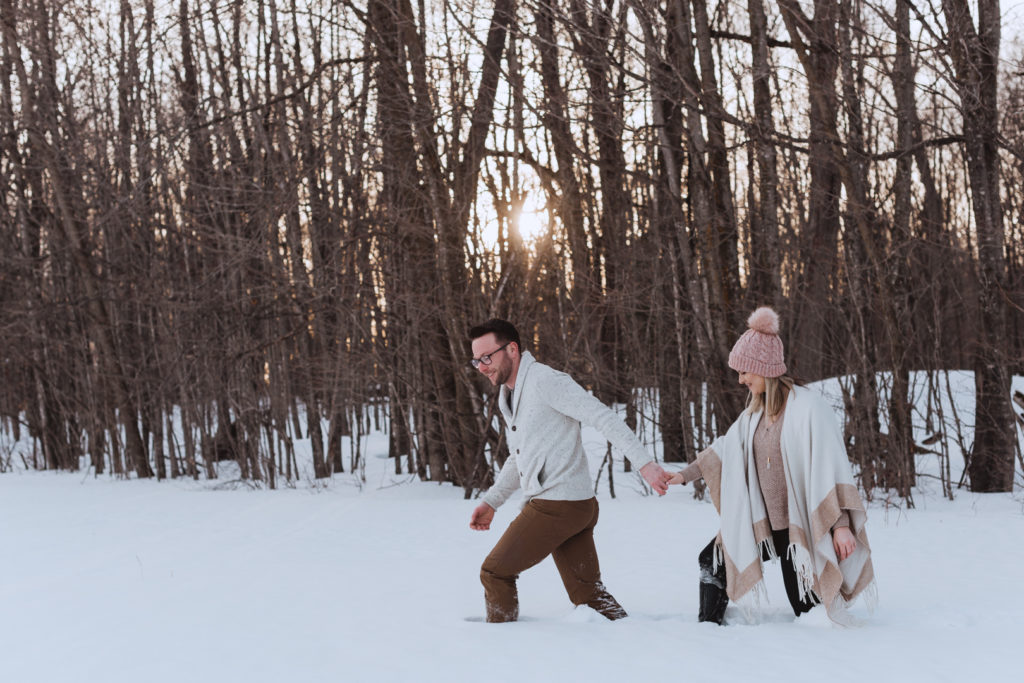 engaged couple walking through the snow in the forest at sunset