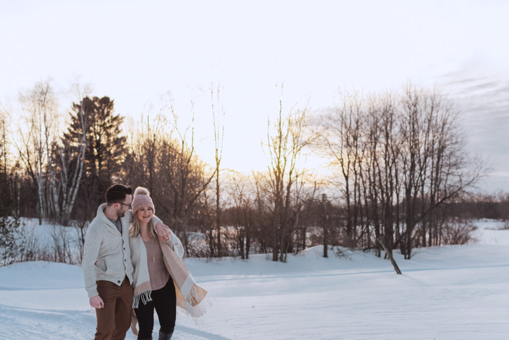 engaged couple walking together in a snowy field at sunset