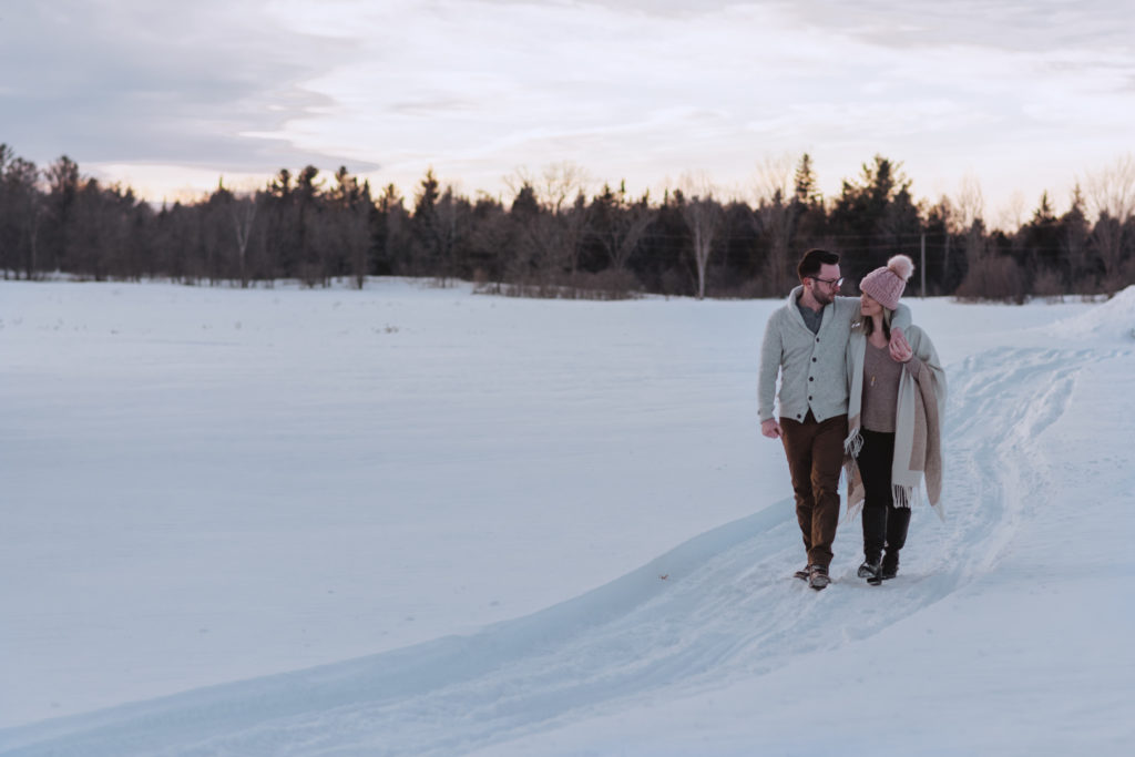 engaged couple walking down a snowy trail at sunset
