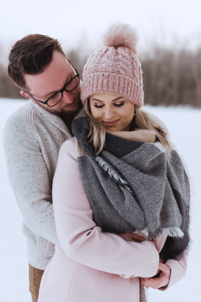 engaged couple cuddling in a snowy field