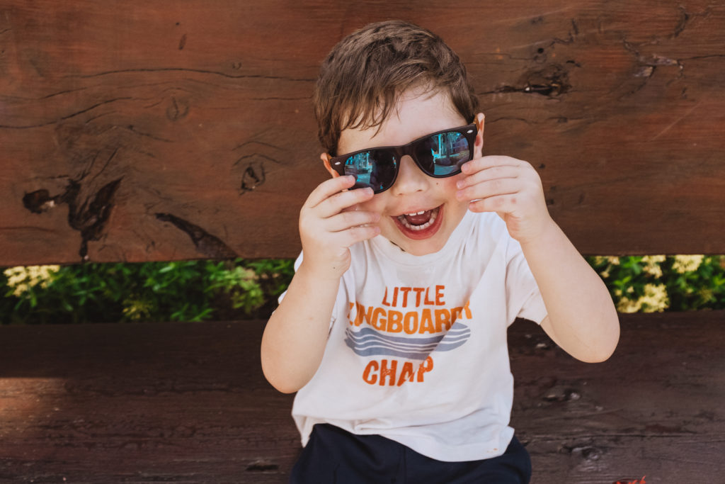 boy sitting on a bench laughing with sunglasses on