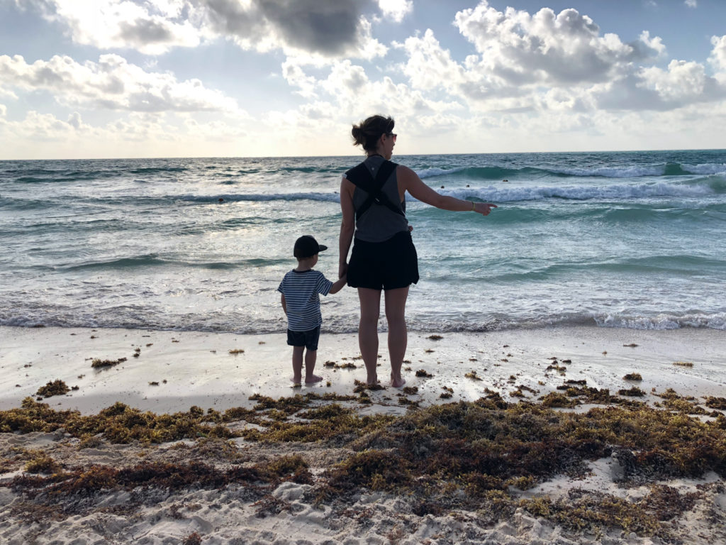 mom holding toddler's hand looking at the ocean