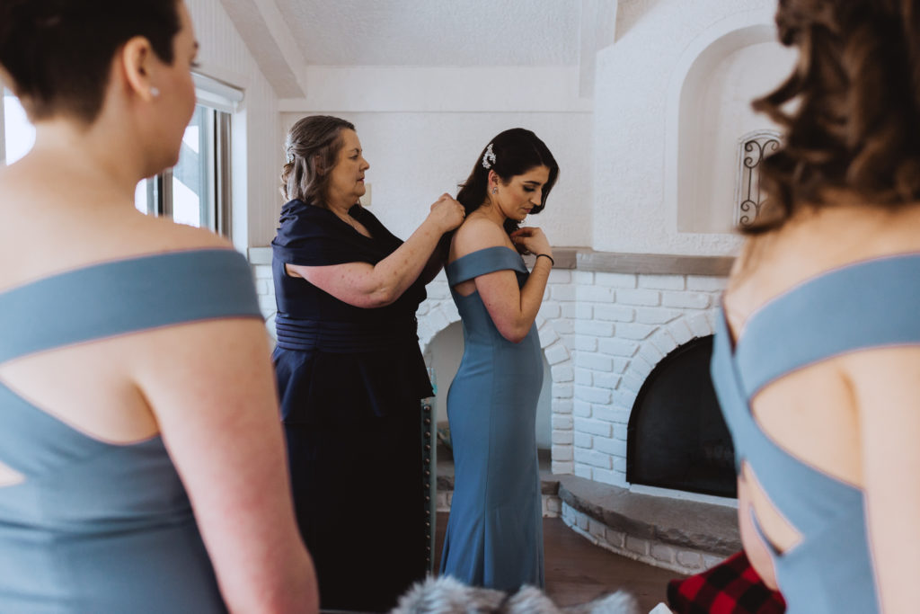 mother of the bride helping bridesmaid put on her necklace