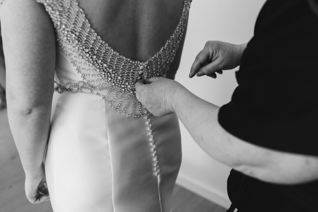 mother of the bride tying up buttons on back of wedding dress