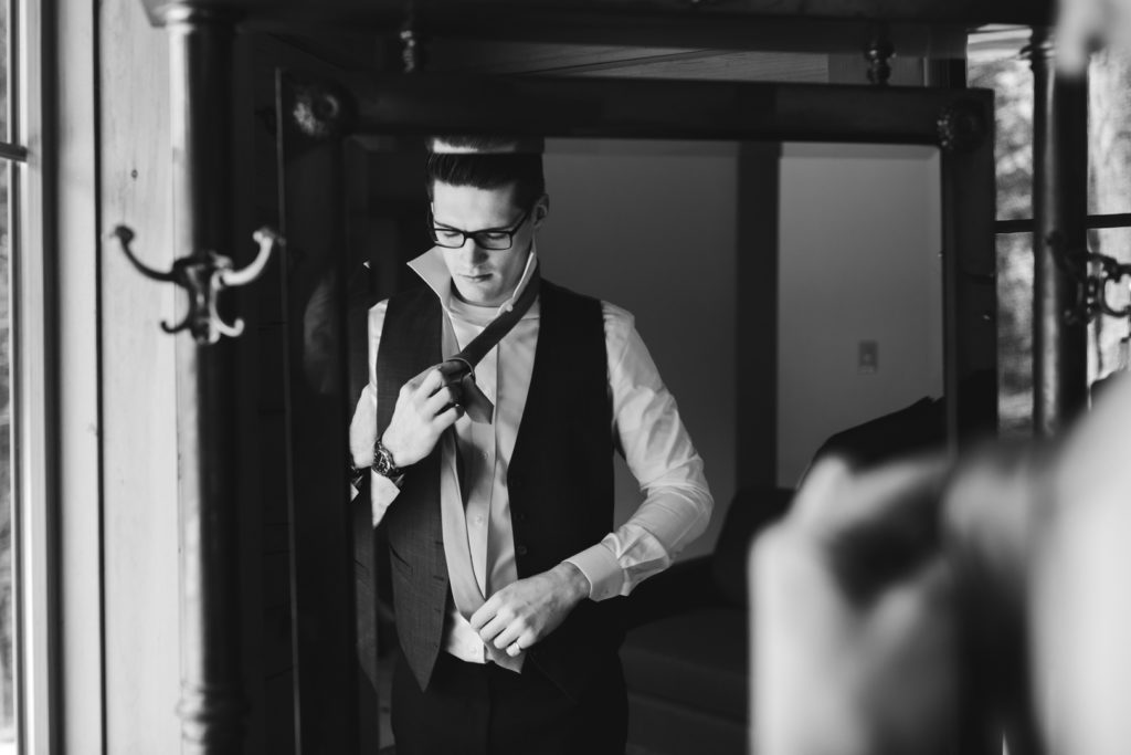 groom putting on his tie in the mirror