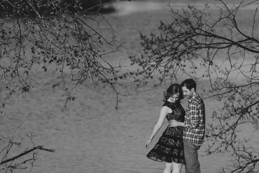 black and white photo of couple standing under trees while dress blows in the wind
