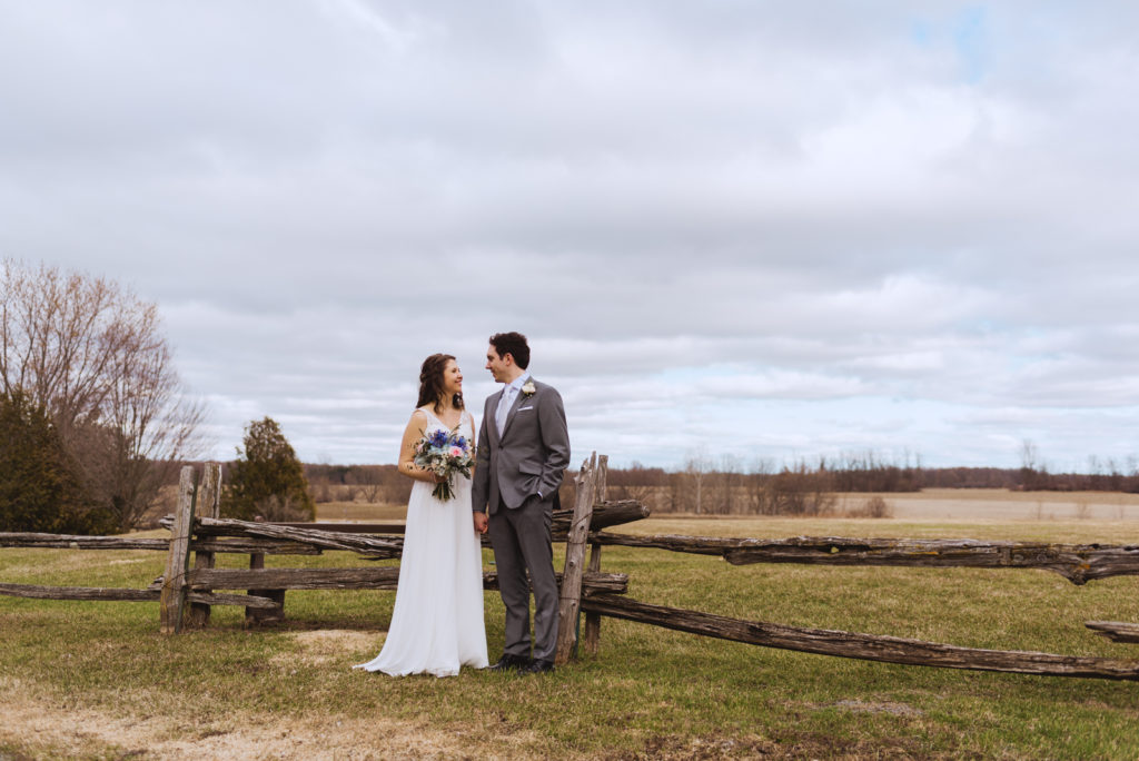 bride and groom in front of wooden fence in a field