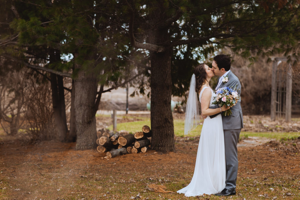 bride and groom kissing by stacks of logs