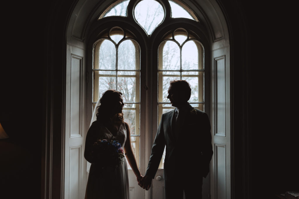 silhouette of bride and groom holding hands by window