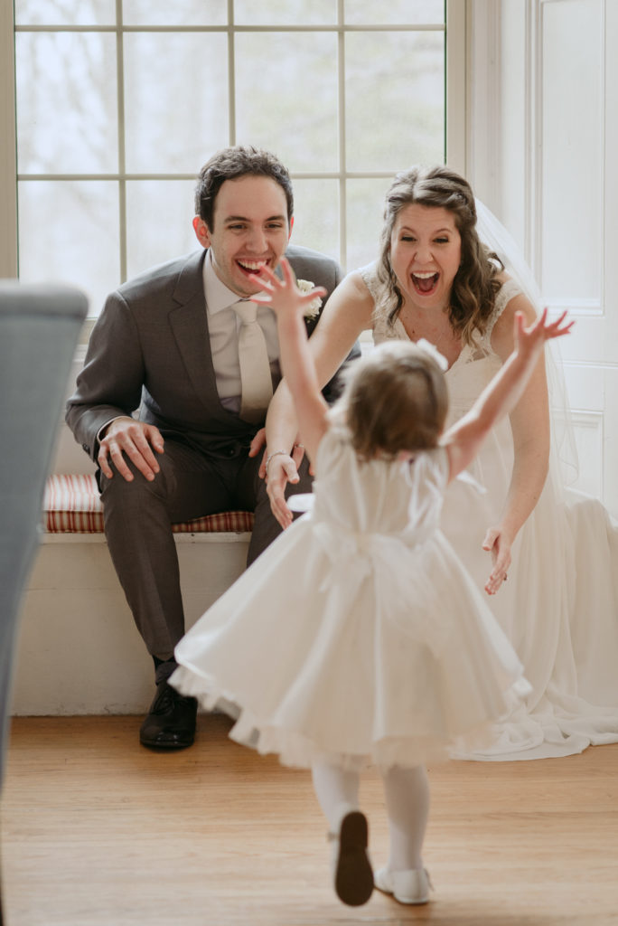 bride and groom laughing as their daughter runs towards them