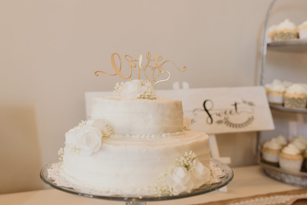 white wedding cake with gold cake topper that says 'love'