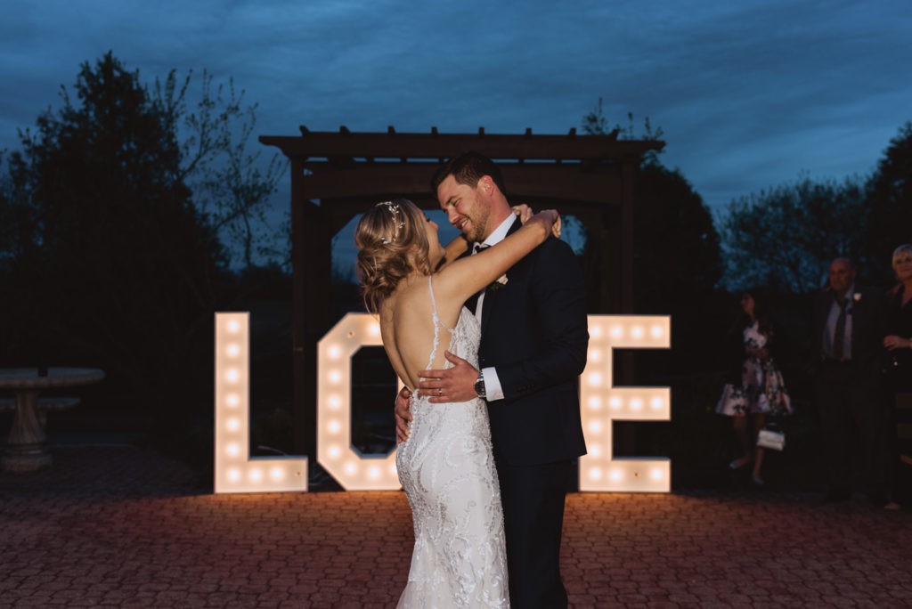 bride and groom first dance outside in front of "love" neon sign