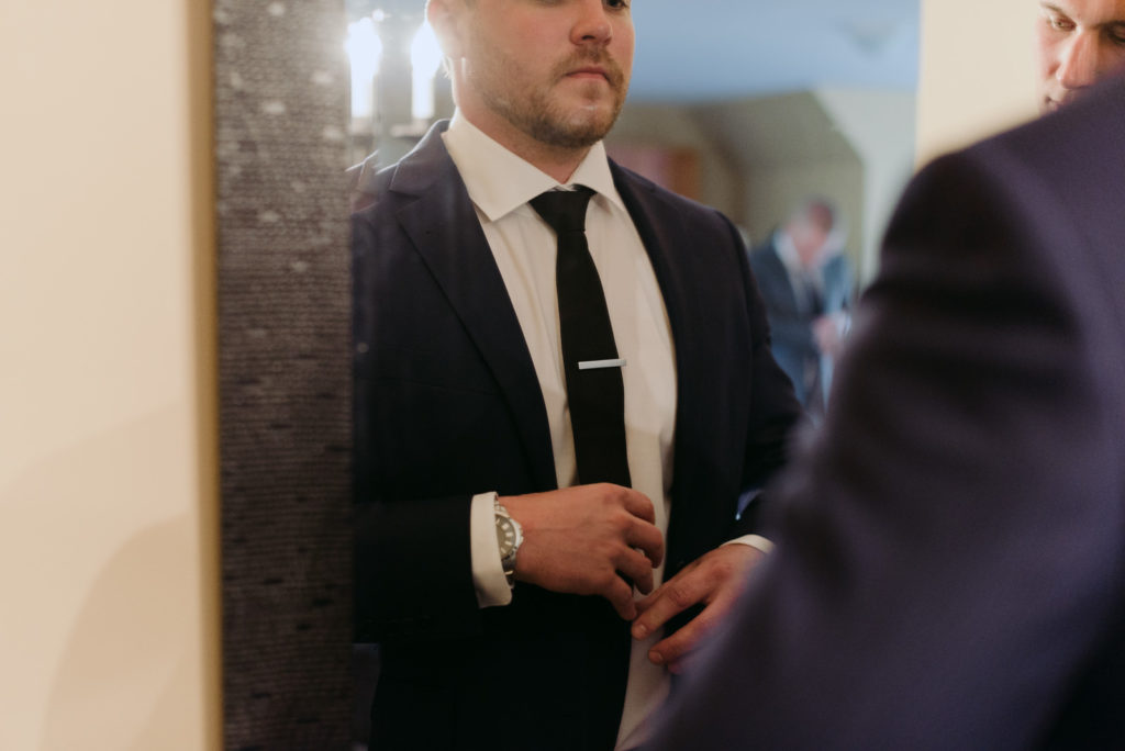 groom adjusting tie in the mirror