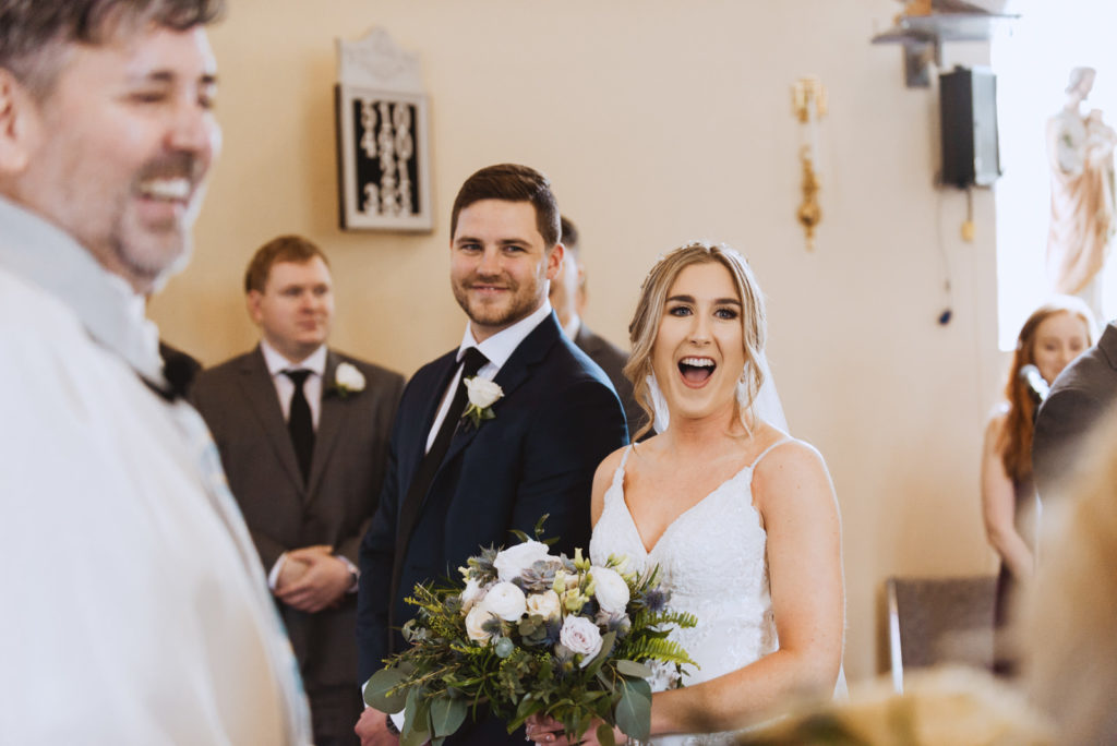 bride and groom laughing with the priest at church wedding
