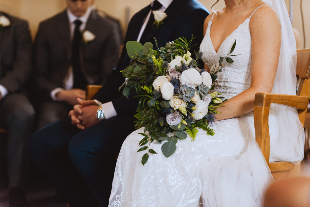 bride holding wild bouquet sitting in a chair at church wedding