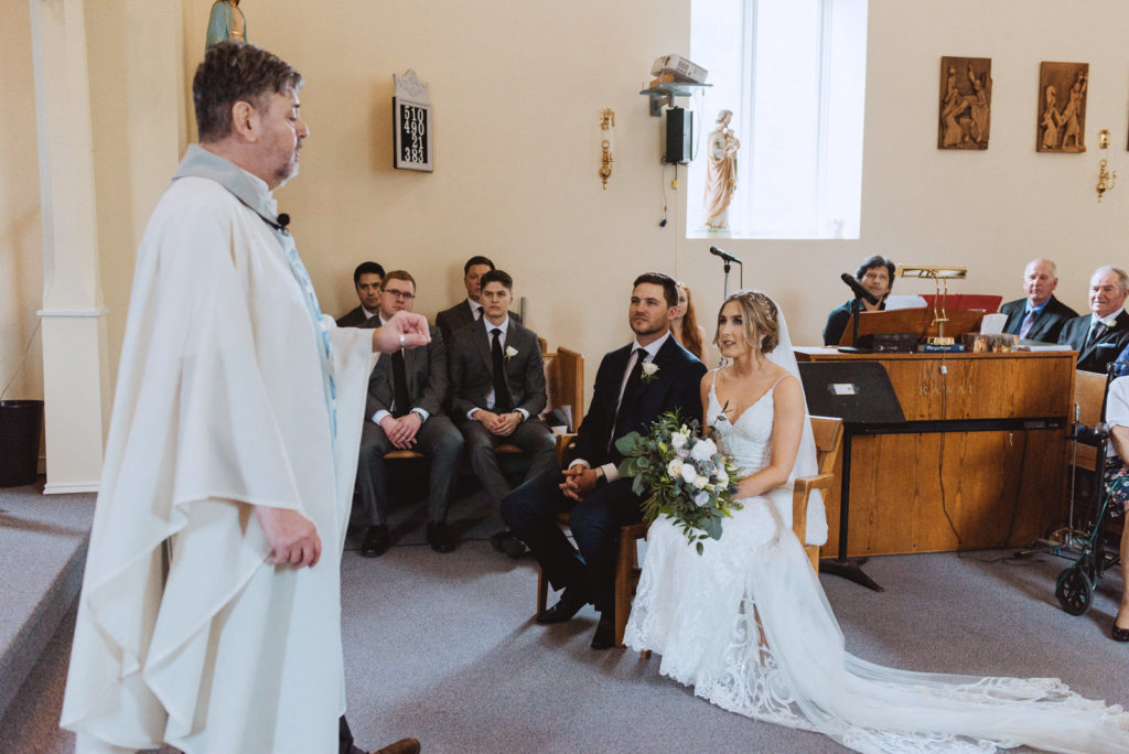 bride and groom listening to priest deliver sermon