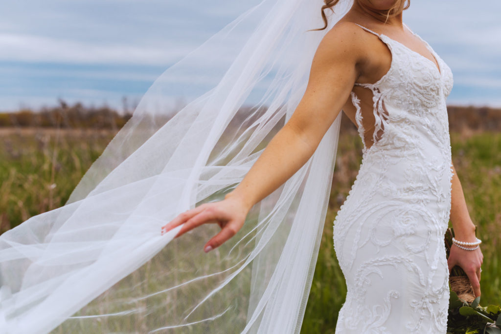 bride playing with her veil in a field as it blows in the wind