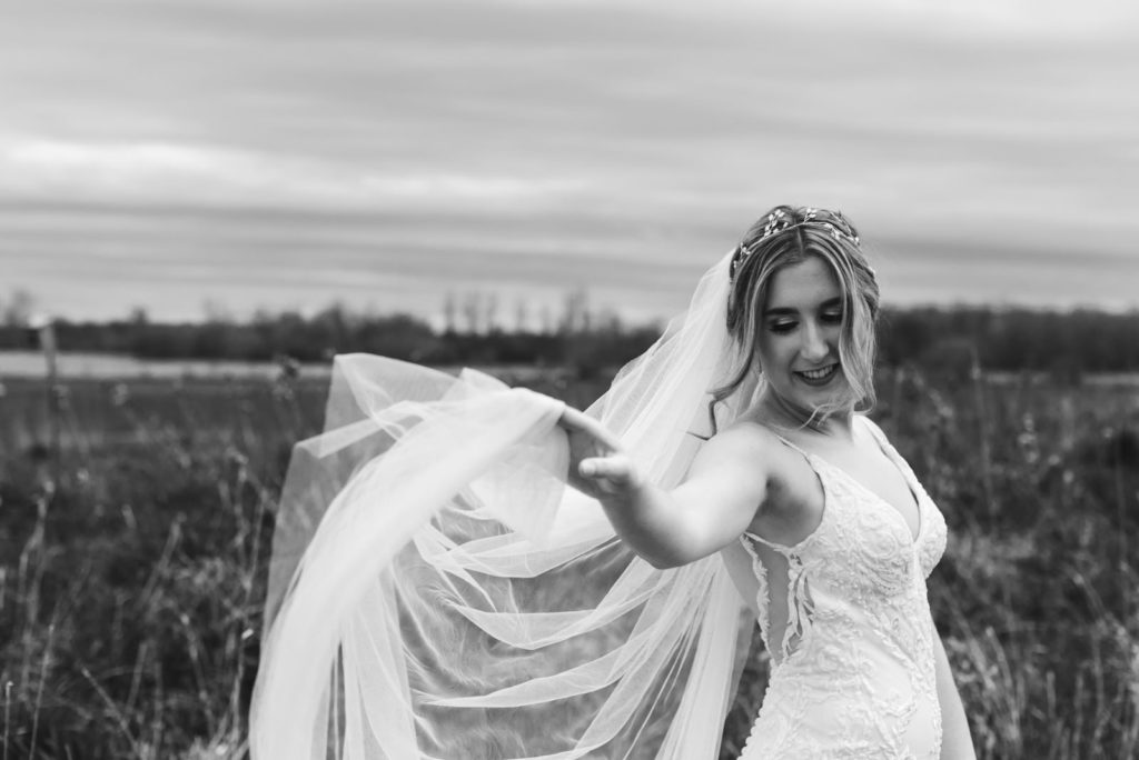 black and white photo of bride playing with her veil in the wind
