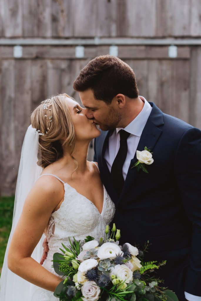 bride and groom kissing in front of wooden barn