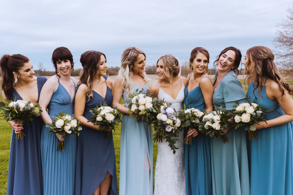 bride and bridesmaids wearing different shades of blue laughing together in the fields of strathmere