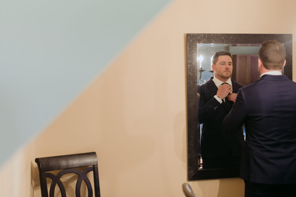 groom adjusting his tie in front of the mirror