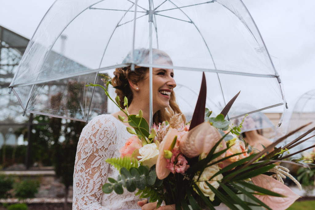 boho bride smiling holding clear umbrella on rainy wedding day