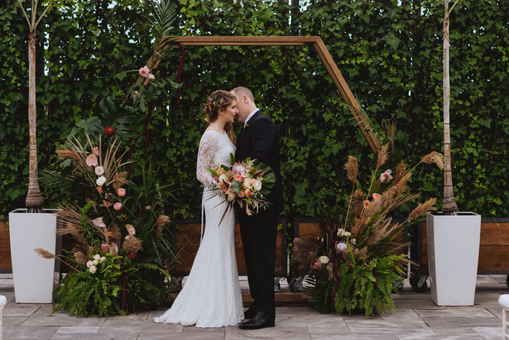 bride and groom under wooden arch at greenhouse wedding