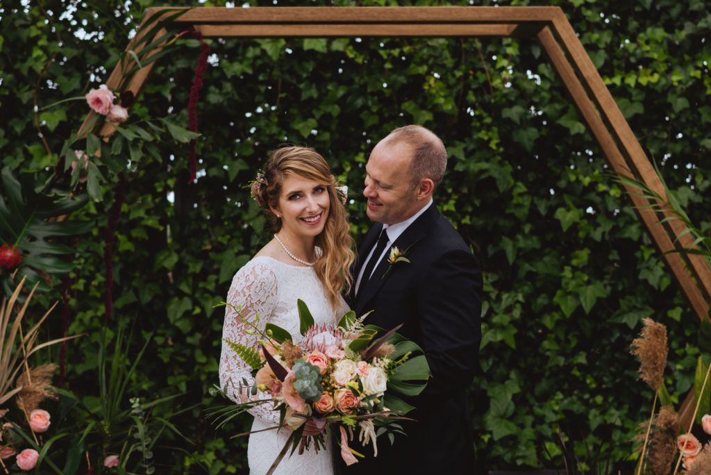 bride and groom under wooden arch at greenhouse wedding