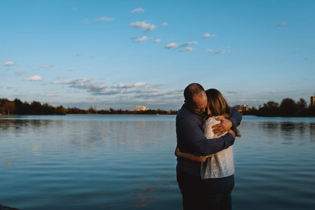 engaged couple hugging each other tight at sunset by the water