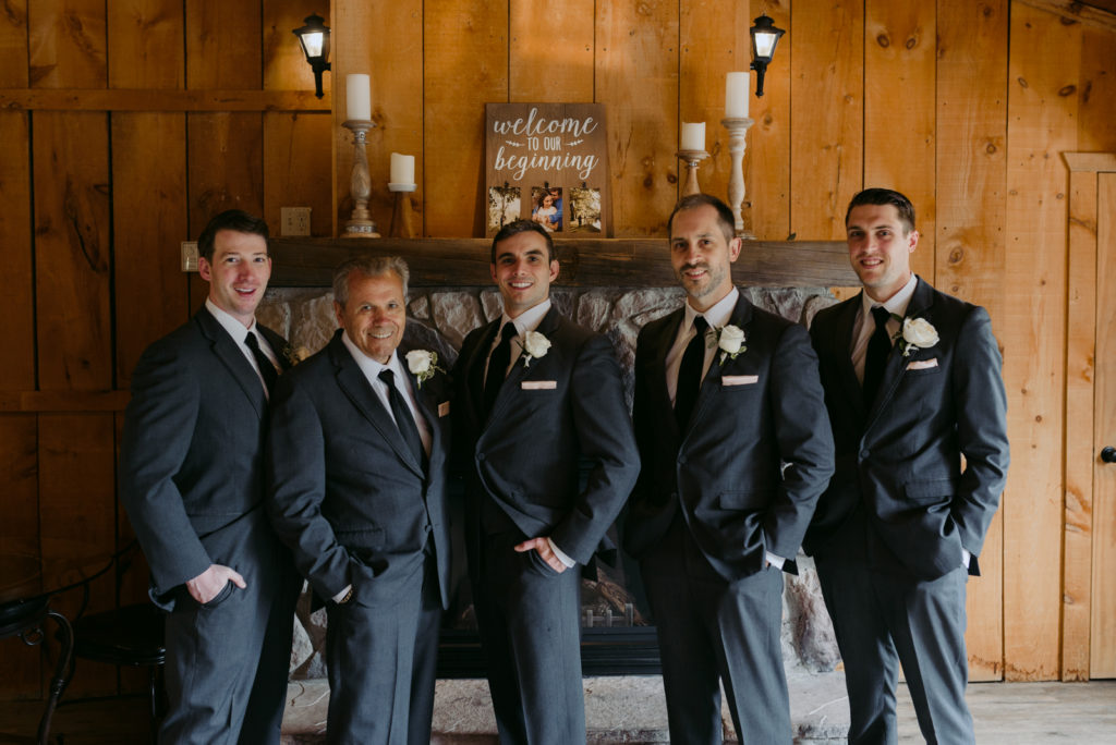 groom and groomsmen by the stone fireplace inside the Strathmere Lodge
