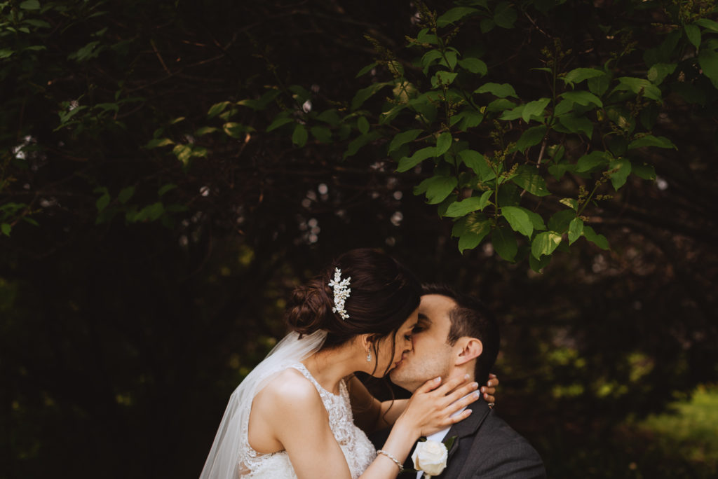 bride and groom kissing underneath trees