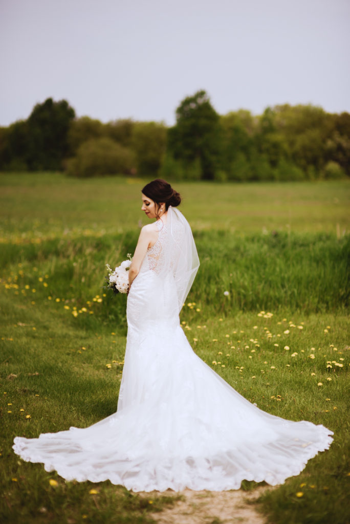 bride standing in a field with train of dress laid out