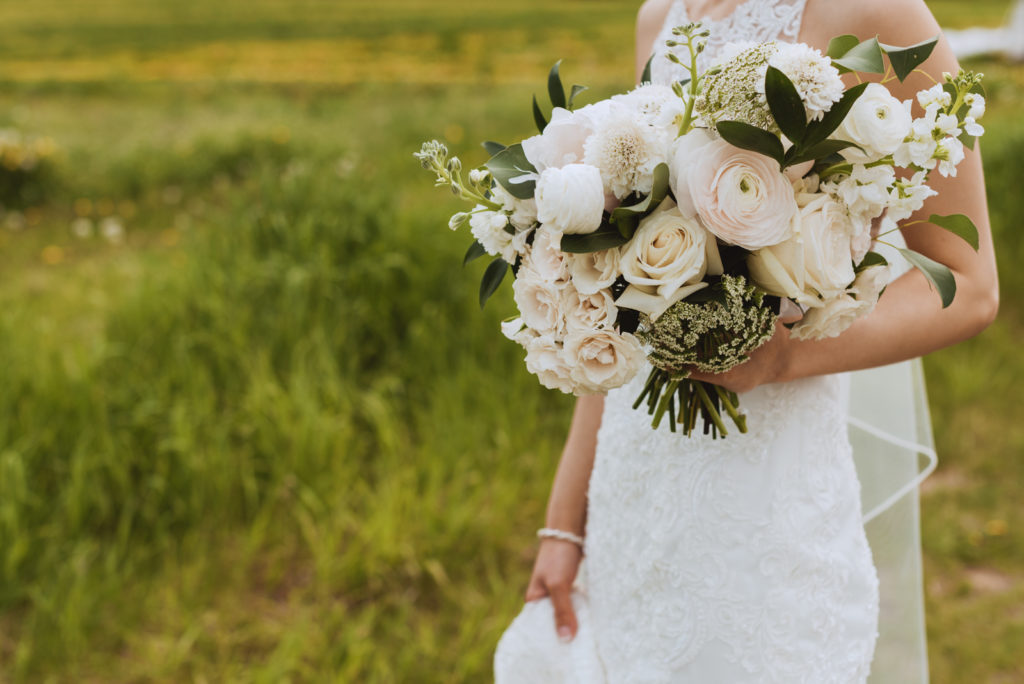 bride holding white and green bouquet in a field