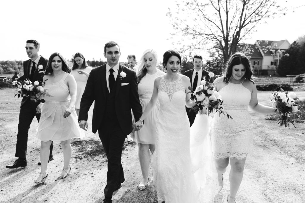 wedding party walking down dirt road laughing