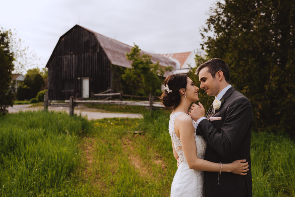 bride and groom cuddling outside of old barn