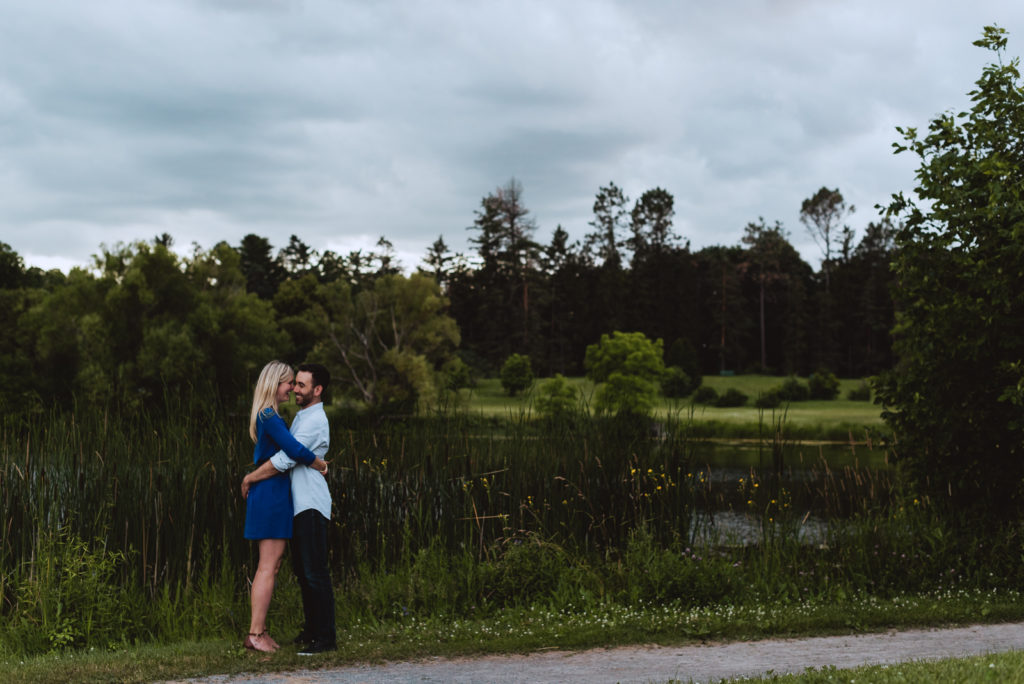 engaged couple by a pond with stormy clouds