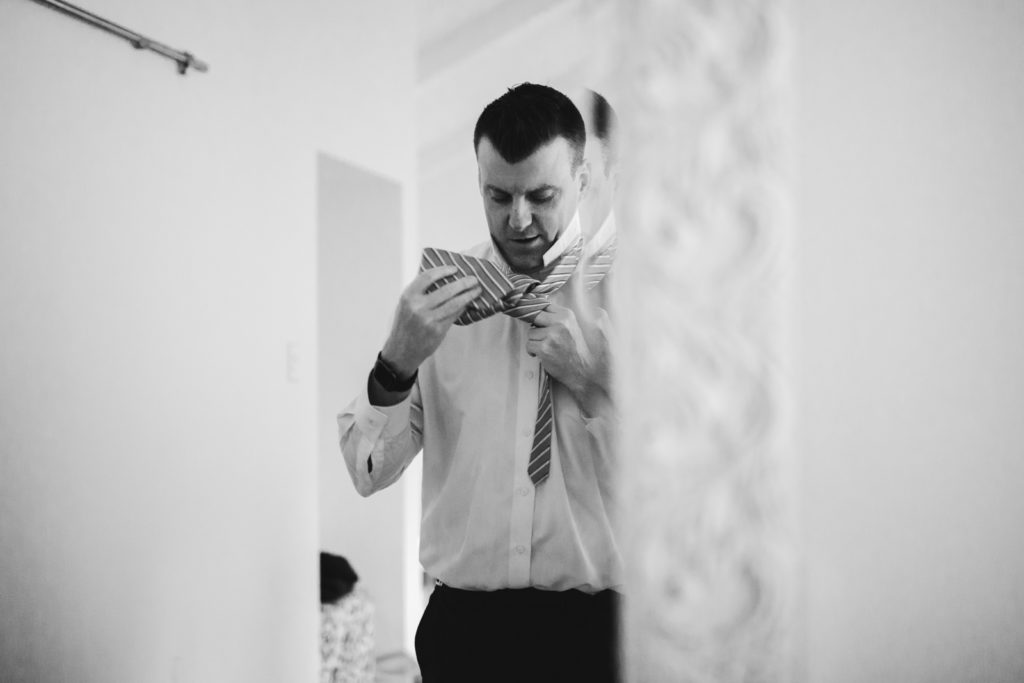 groom putting on his tie in the mirror