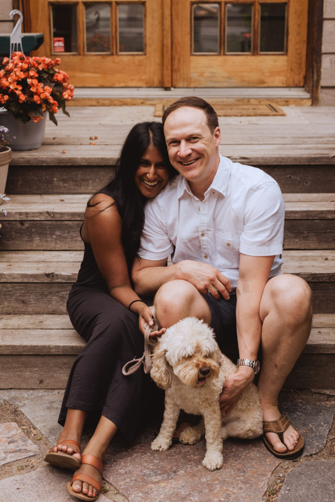 engaged couple sitting on their steps with their schnoodle puppy