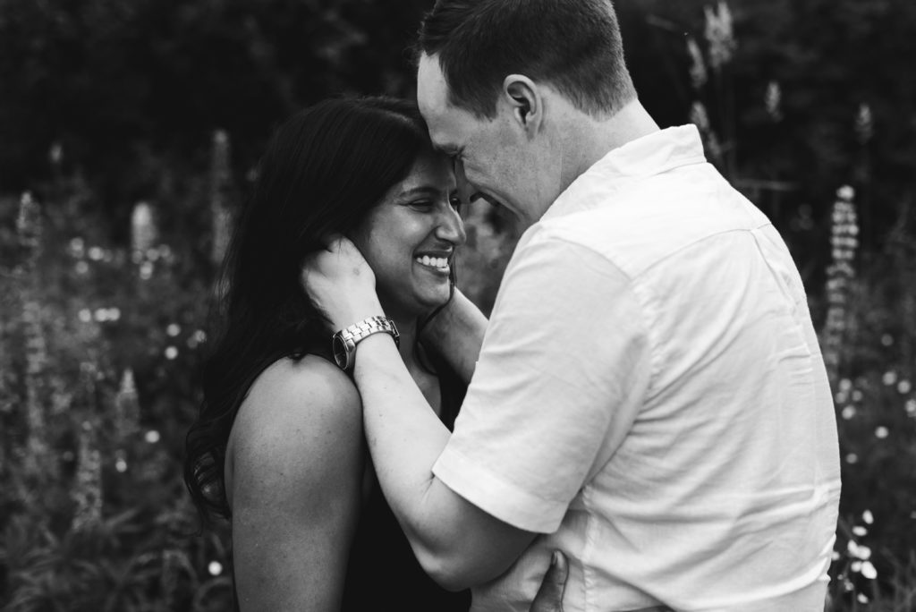 engaged couple cuddling close while laughing in black and white