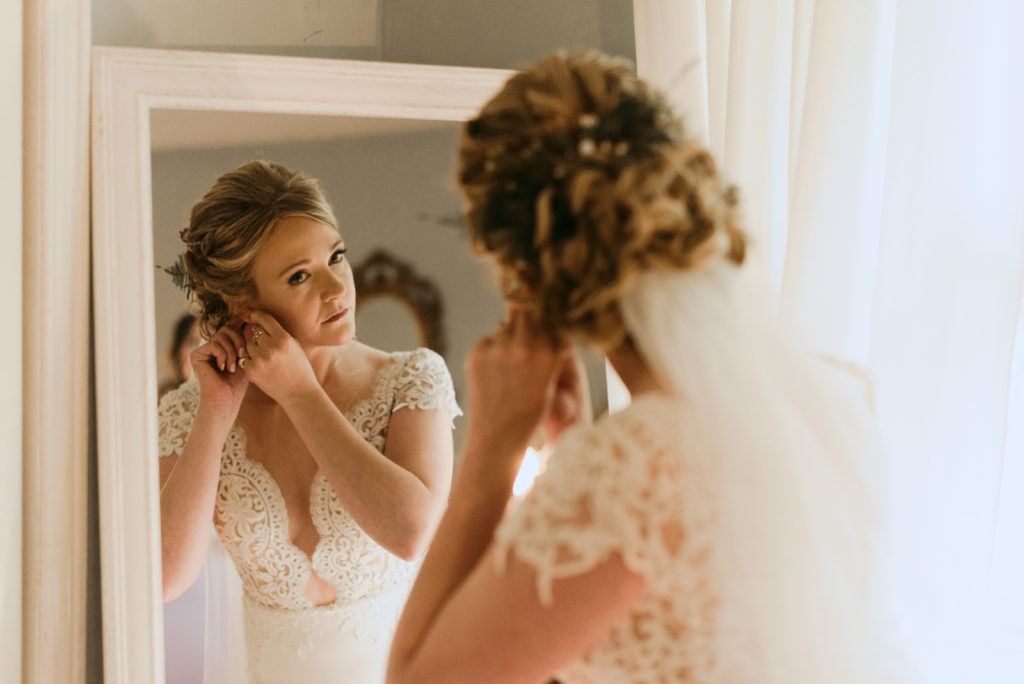 bride putting on her earrings in the mirror