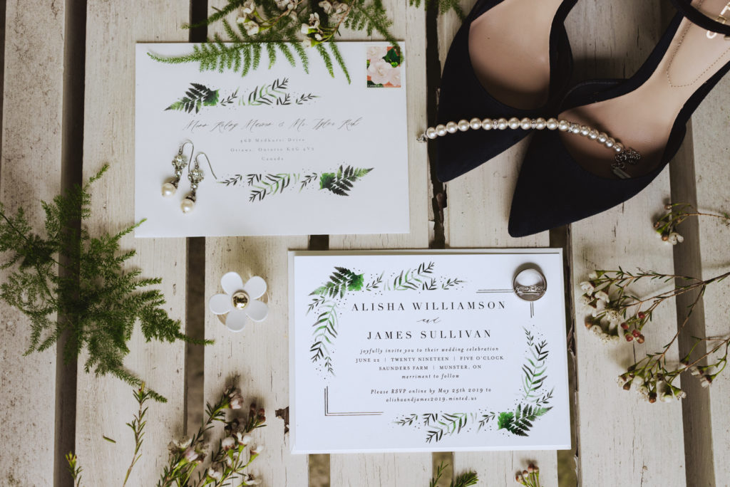 flat lay of invitation suite and wedding jewellery with greenery