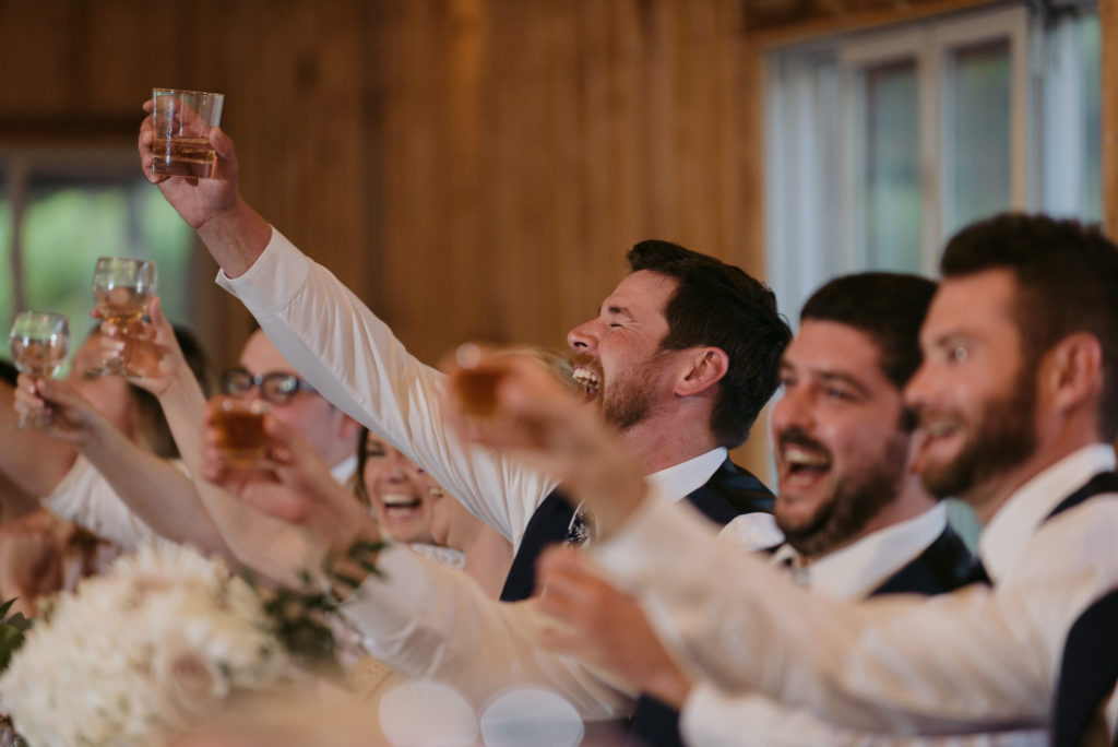 groom laughing and holding up drink during wedding toast