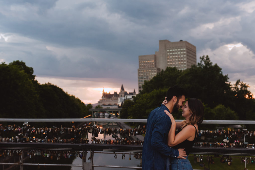 engaged couple on the love lock bridge in Ottawa overlooking the canal at sunset