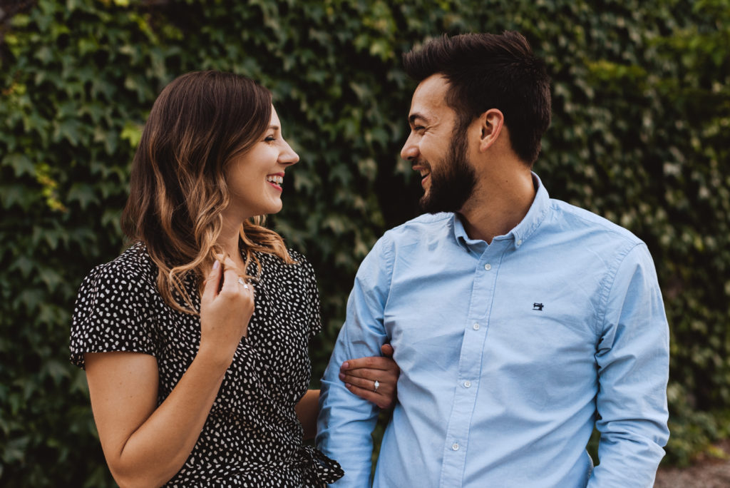 engaged couple laughing in front of wall with vines