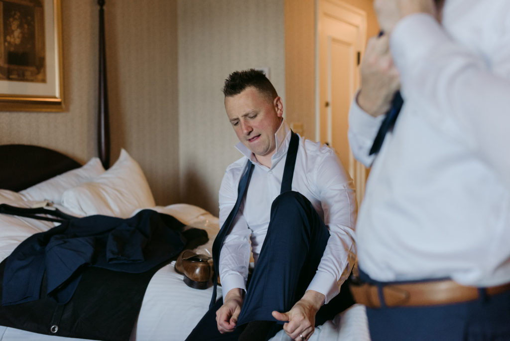groomsman putting on his shoes in hotel room
