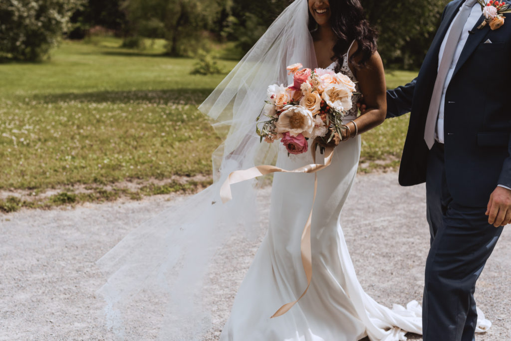 bride and groom walking along dirt trail with bouquet ribbon blowing in the wind