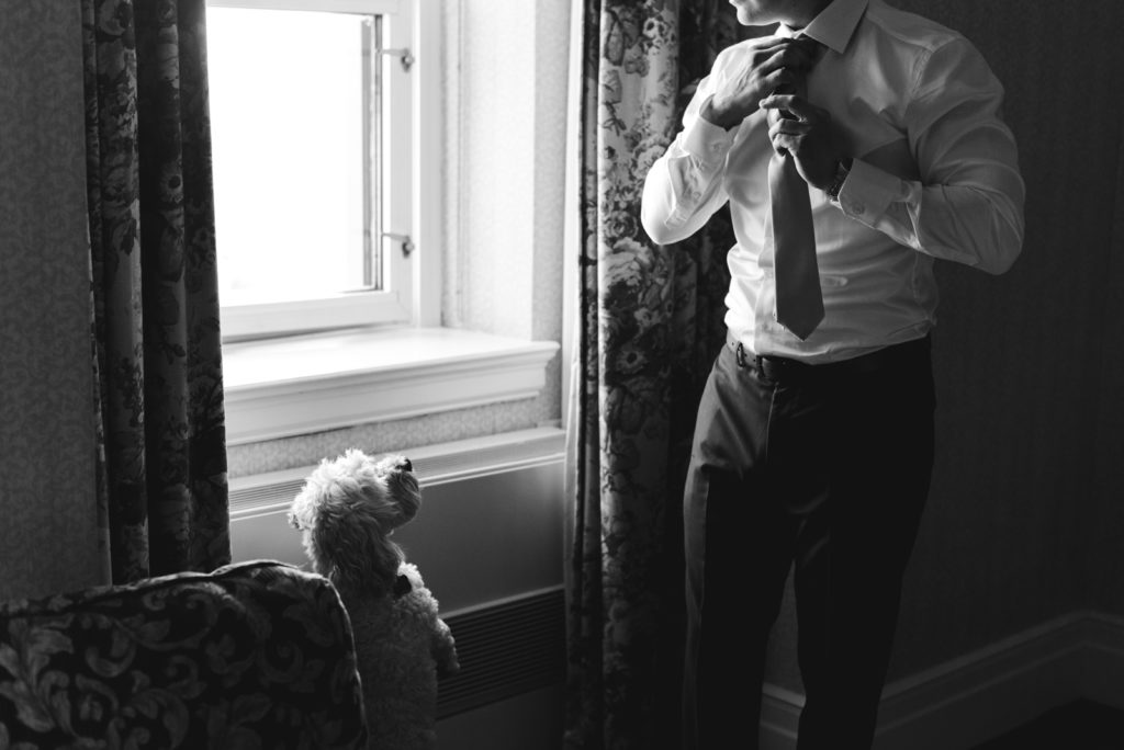 groom adjusting his tie while dog looks at him