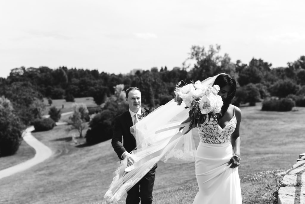 bride and groom walking up hill with cathedral veil blowing in the wind